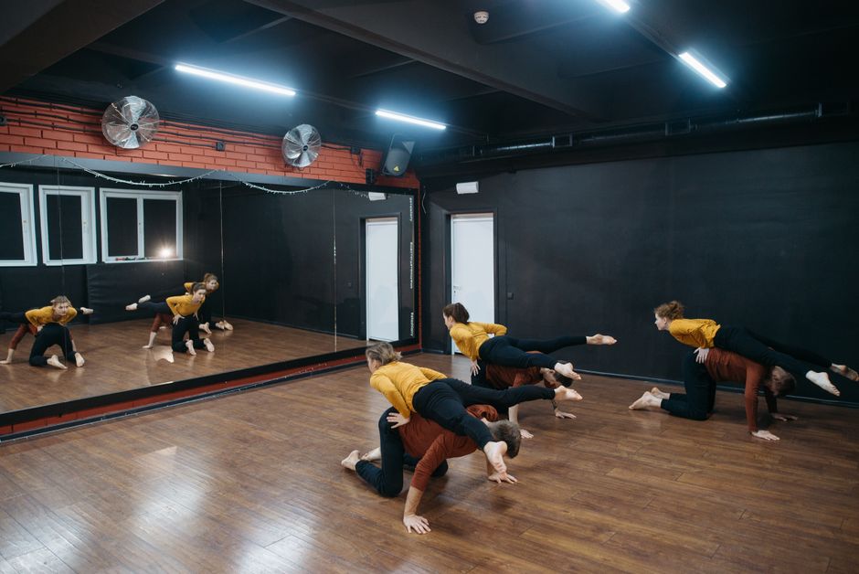Group of dancers rehearsing contemporary choreography in a mirrored studio.