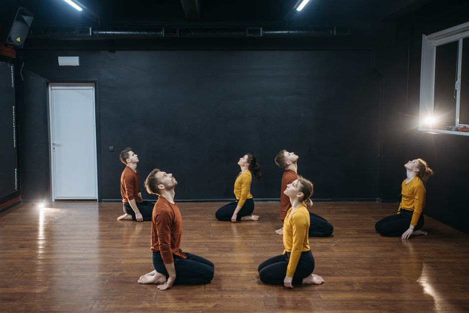 A group of adults rehearsing a contemporary dance routine in a minimalist studio setting.