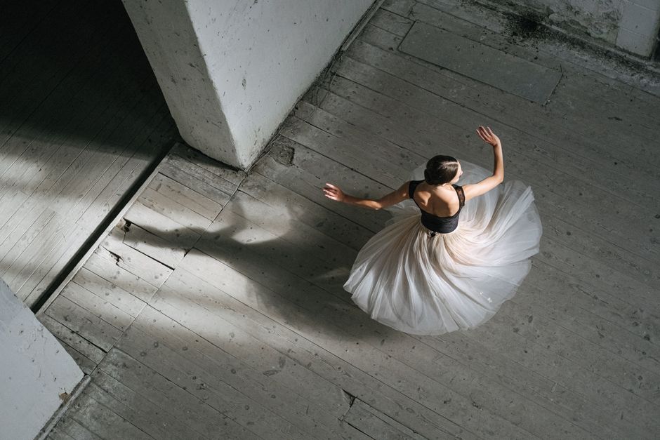 A top-view of a ballerina gracefully spinning in a classic white skirt and black tank top.