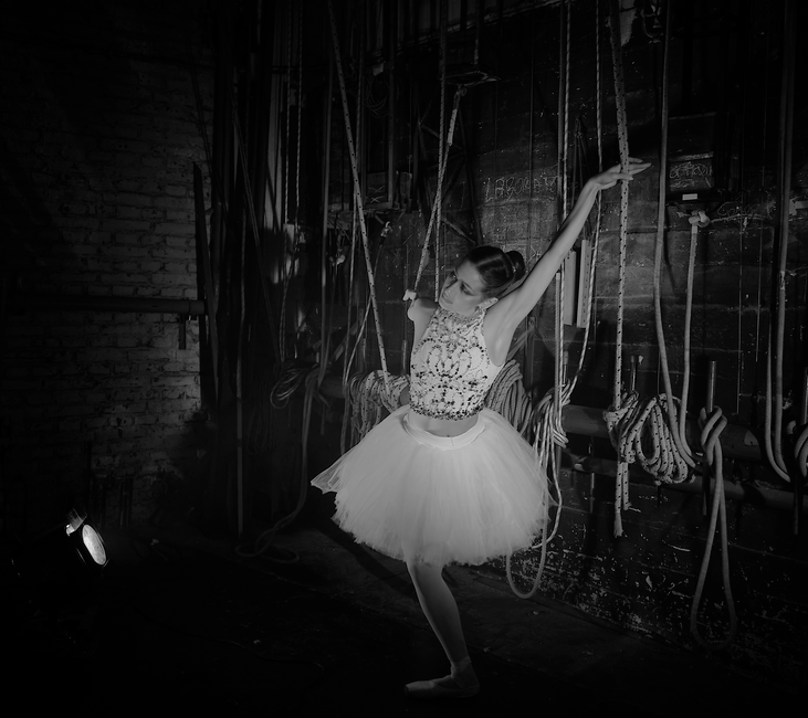 A graceful ballerina striking a pose in a dramatic backstage environment.